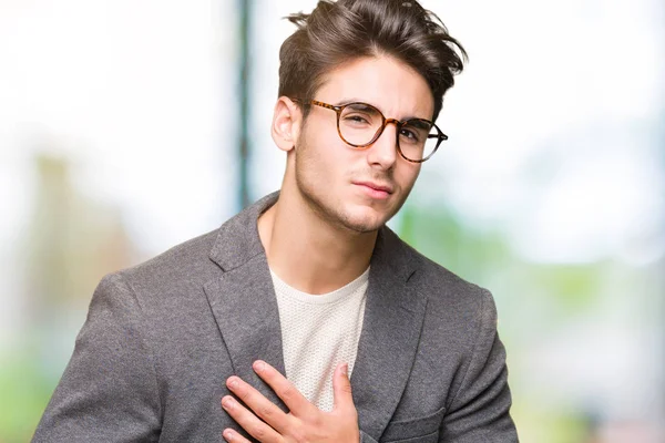 Young business man wearing glasses over isolated background with hand on stomach because indigestion, painful illness feeling unwell. Ache concept.