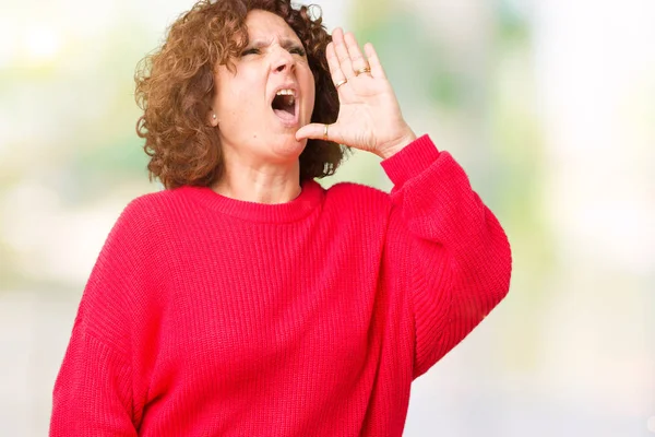 美丽的中间年龄的老年妇女红色冬季毛衣在孤立的背景大喊和尖叫到一边的手在嘴 沟通理念 — 图库照片