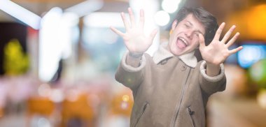 Gösterilen arka plan üzerinde kış ceket giyen genç yakışıklı adam izole ve parmakları ile işaret kendinden emin ve mutlu gülümseyerek süre on numara.