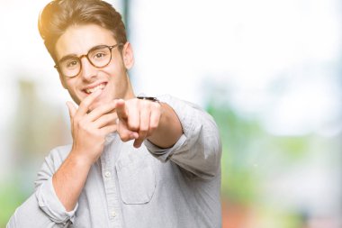 Genç yakışıklı adam gözlük izole üzerinde gülme sizin parmak el kamerasıyla ağzına, utanç ifadesi işaret eden arka plan