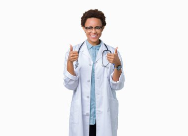 El ile pozitif jest yapıyor izole arka plan başarı işareti üzerinde tıbbi ceket giyen genç Afro-Amerikan doktor kadın başparmak gülümseyen ve mutlu. Neşeli bir ifadeyle, kazanan jest kameraya bakıyor.