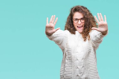 Güzel esmer kıvırcık saçlı Genç kız giyiyor kış kazak gösterilen ve parmakları ile işaret izole arka plan üzerinde kendinden emin ve mutlu gülümseyerek süre on numara.