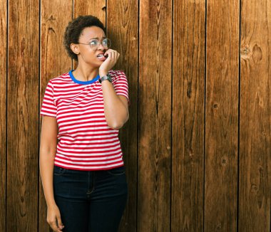 Stresli ve gergin elle çivi ısırma ağzına bakarak izole arka plan üzerinde gözlük güzel genç Afro-Amerikan kadın. Anksiyete sorunu.