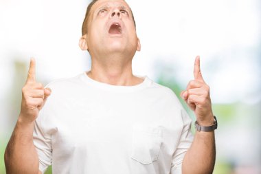 Orta yaş Arap adam aşınmış beyaz t-shirt üzerinde izole arka plan hayran ve sürpriz bakarak ve parmaklar ve yükseltilmiş silah ile işaret.