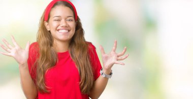 Üzerinde kırmızı t-shirt giyen genç güzel esmer kadın deli kutluyor arka plan izole ve silah ile başarı için yükseltilmiş ve açık gözleri heyecanlı çığlık hayrete düşürdü. Kazanan kavramı