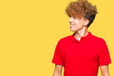 Uzak tarafına yüzünde, doğal ifade gülümseme ile seyir kırmızı t-shirt giyen afro saçlı genç yakışıklı adam. Kendine güvenen gülüyor.