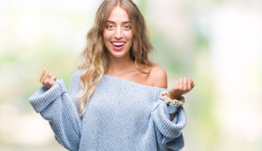 İzole arka plan üzerinde kutluyor kış kazak giyen güzel genç sarışın kadın şaşırttı ve başarı için kaldırdı kollarını açarak hayret ve gözleri açık. Kazanan kavramı.