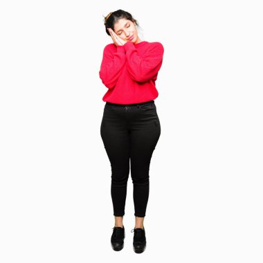 Rüya ve elleri ile kapalı gözler gülümseyen birlikte poz kırmızı kazak ve topuz uyku giyen genç güzel kadın yorgun.