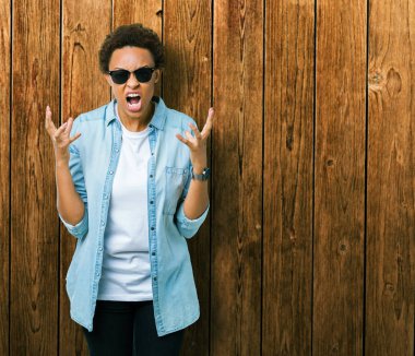 Güzel genç Afro-Amerikan kadın üzerinde güneş gözlüğü takıyor arka plan deli izole ve deli bağırarak ve agresif ifade ve silah kaldırdı bağırıyor. Hayal kırıklığı kavramı.