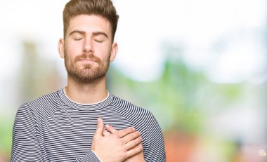 Yakışıklı delikanlı ile gülümseyen çizgili Süveter giyen kapalı gözler ve yüzünde minnettar jest ile göğüs üzerinde eller. Sağlık kavramı.