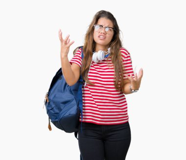 Genç güzel esmer öğrenci kadın izole arka plan üzerinde kulaklık ve sırt çantası giyiyor deli ve deli çığlık ve agresif ifade ve silah ile bağırdı kaldırdı. Hayal kırıklığı kavramı.