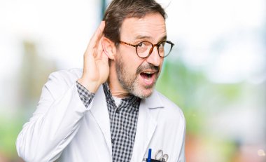 Orta yaş doktor erkek ile gülümseyen bir tıbbi palto giyiyor bir işitme söylenti ya da dedikodu için dinleme kulak teslim. Sağırlık kavramı.