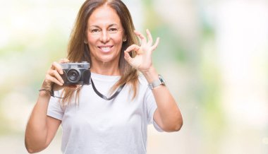 Orta yaş İspanyol kadın parmakları, mükemmel sembolü olan ok işareti yapıyor izole arka plan üzerinde Vintage Fotoğraf kamera ile fotoğraf çekmek