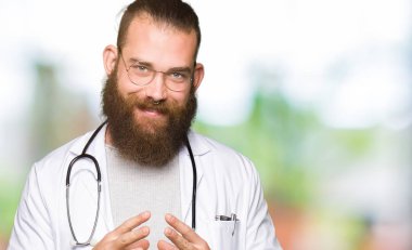 Genç Sarışın Doktor adam tıbbi kat eller birlikte giyen sakal ve parmakları ile rahat ve neşeli gülümseyen geçti. Başarı ve iyimser