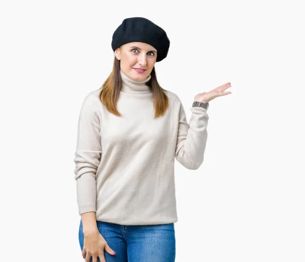 中年成熟的女人穿着冬季毛衣和贝雷帽在孤立的背景微笑欢快的呈现和指着手掌看着相机 — 图库照片