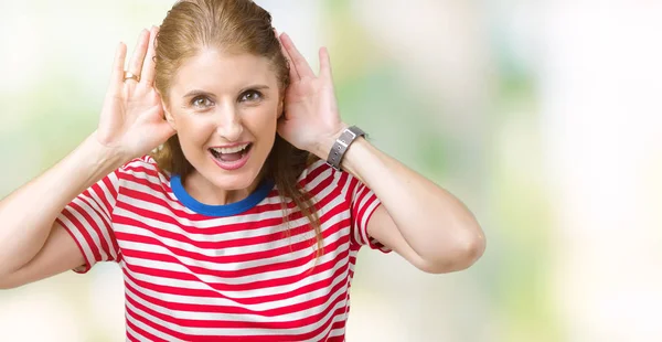 中年成熟的女人穿着休闲 T恤在孤立的背景试图听到双手对耳朵的手势 好奇八卦 听力问题 — 图库照片