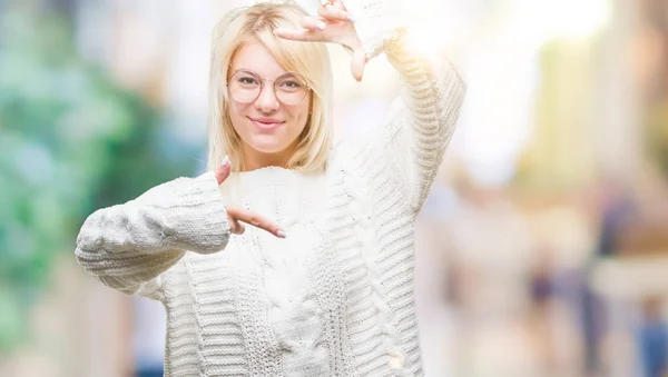 若い美しい金髪女性の笑顔の幸せそうな顔で指と手作りフレーム分離の背景に冬のセーターとメガネを着用します 創造性と写真のコンセプト — ストック写真