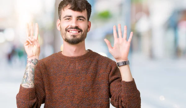 Gösterilen arka plan üzerinde kış kazak giyen genç yakışıklı adam izole ve parmakları ile işaret kendinden emin ve mutlu gülümseyerek süre 8 numaralı.