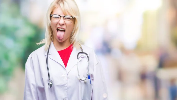 年轻美丽的金发碧眼的医生妇女穿着医疗制服在孤立的背景伸出舌头出来快乐与搞笑的表情 情感概念 — 图库照片