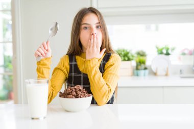 Güzel genç kız çocuk yemek çikolata tahıl ve süt için kahvaltı kapağı ağız ile el hata için utanç ile şok, korku ifade, sessizlik, gizli kavramı korkuyor