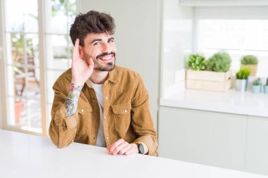 Beyaz masada oturan rahat ceket giyen genç adam kulak üzerinde el ile gülümseyen söylenti veya dedikodu bir işitme dinlerken. Sağırlık konsepti.