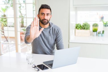 İspanyol yakışıklı çalışma açık eliyle dur işareti ile ifade, ciddi ve kendinden emin yaparken bilgisayar dizüstü kullanarak savunma hareketi