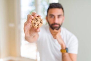 Yakışıklı İspanyol adam yemek çikolata cips çerezler ciddi yüz soru hakkında düşünme, çok karışık fikir