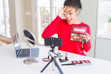 Genç African American etki unsuru kadın kayıt mutlu yüz gülümseyen ile öğretici parmak görünümlü göz el ile ok işareti yapıyor makyaj