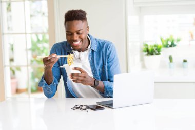 Gülümseyen erişte zevk teslim Asya yemek yiyor ve bilgisayar kullanılarak yakışıklı genç Afrika iş adamı