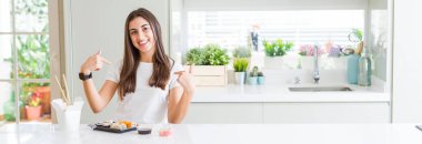 Güzel genç kadının teslim Asya Suşi yeme geniş açı resim yüzünde gülümseme ile kendine güvenen görünümlü, parmaklarıyla gurur ve mutlu kendini işaret.