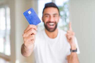 Yakışıklı İspanyol adam tutan kredi kartı bir fikir veya soru mutlu yüz, bir numara ile parmak işaret ile şaşırttı