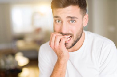 Evde rahat beyaz t-shirt giyen genç yakışıklı adam vurguladı ve ağız ısırma çivi elleri ile gergin bakıyor. Anksiyete sorunu.