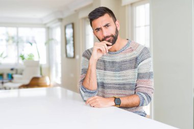 Çene düşünme hakkında soru, dalgın ifade üzerine el ile evde rahat kazak giyen yakışıklı İspanyol adam. Düşünceli yüzüyle gülümsüyor. Şüphe kavramı.