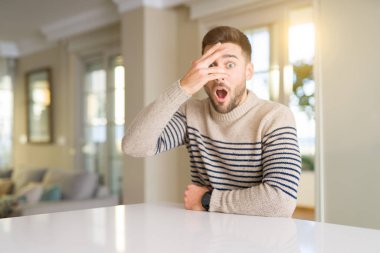 Evde Genç yakışıklı adam şok kapsayan yüz ve gözleri el ile göz, utanmış ifade ile parmaklar bakarak.