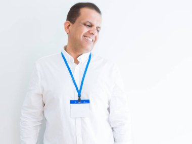 Orta yaş iş adamı beyaz arka plan uzak tarafına gülümseme ile yüzünde, doğal ifade bakmaktan kimlik kartı takıyor. Kendine güvenen gülüyor.