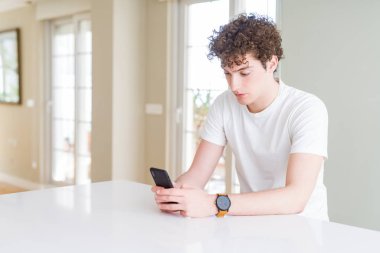 Genç adam akıllı yüzünde ciddi düşünme emin bir ifade ile evde Smartphone kullanarak