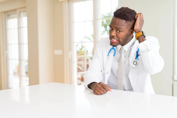 African american doctor man at the clinic confuse and wonder about question. Uncertain with doubt, thinking with hand on head. Pensive concept.
