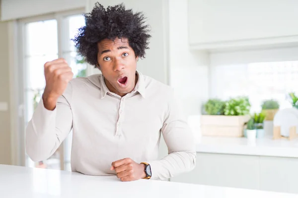 African American man at home angry and mad raising fist frustrated and furious while shouting with anger. Rage and aggressive concept.