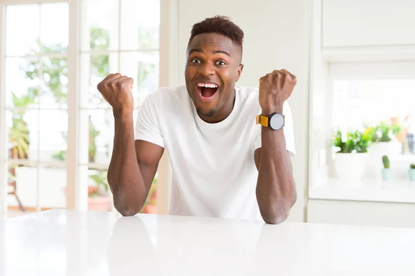 白いテーブル自宅でハンサムなアフリカ系アメリカ人は腕を上げると 驚きと驚きの成功を祝うと目を開きます 勝者の概念 — ストック写真