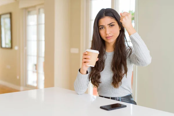 Young woman drinking a cup of coffee at home annoyed and frustrated shouting with anger, crazy and yelling with raised hand, anger concept