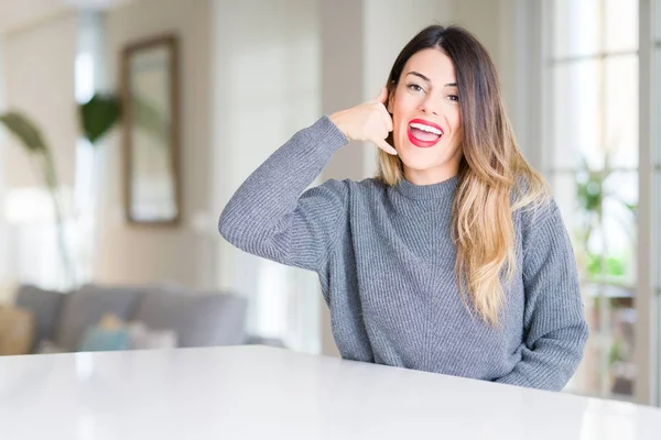 Young beautiful woman wearing winter sweater at home smiling doing phone gesture with hand and fingers like talking on the telephone. Communicating concepts.