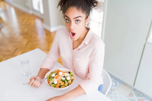 年轻的非洲裔美国妇女吃健康的意大利面沙拉吓得惊讶与一个惊喜的脸 害怕和兴奋的恐惧表情 — 图库照片
