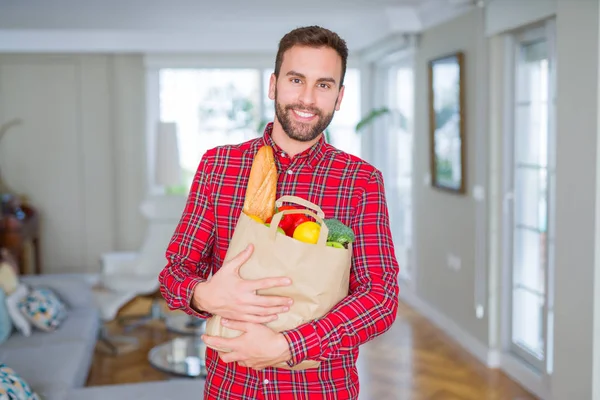 Handsome man holding groceries bag with a happy face standing and smiling with a confident smile showing teeth