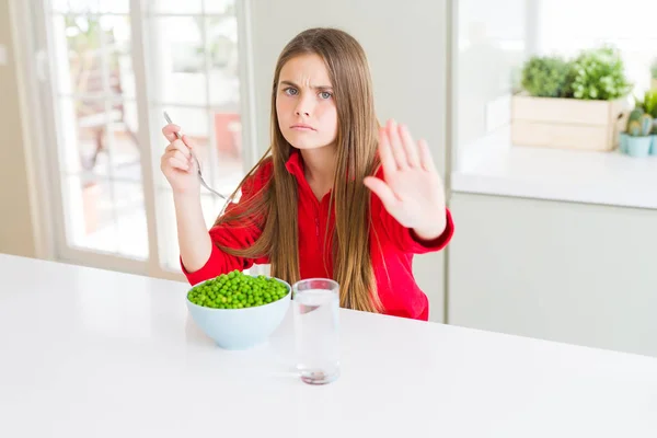 美しい若い女の子が開いた手で健康的なグリーンピースを食べることは 深刻で自信を持った表現 防衛ジェスチャーで停止標識 — ストック写真