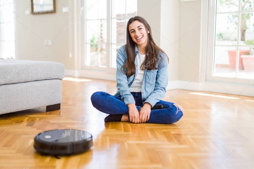 Young woman using automatic vacuum cleaner to clean the floor, controling machine housework robot