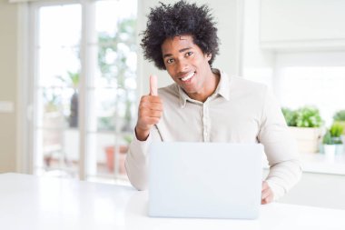 Afrika kökenli Amerikalı adam çalışma dizüstü mutlu ok işareti yapıyor büyük gülümseme ile kullanma başparmak yukarı parmaklarıyla, mükemmel işareti