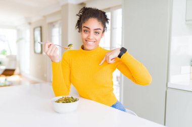 Genç Afrikalı Amerikan kadın kendini sürpriz yüz işaret parmak ile sağlıklı yeşil sebze yeme