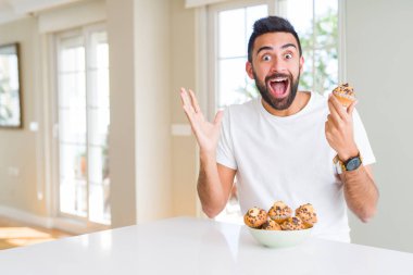 Kocaman bir gülümseme ile çığlık ve ellerini kaldırdı muffin çok mutlu ve heyecanlı, kazanan ifade kutluyor zafer yakışıklı İspanyol adam yeme çikolata cips