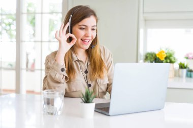 Laptop ile çalışma ve parmak, mükemmel sembolü ile ok işareti yapıyor headseat giyen güzel genç operatör kadın