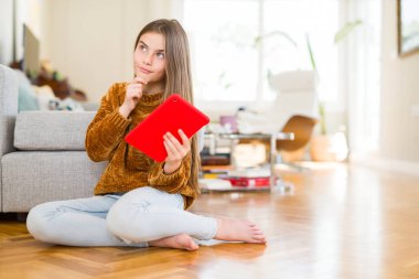 Güzel genç kız çocuk yerde ciddi bir yüz düşünme hakkında soru, çok karışık bir fikir üzerine oturan dijital dokunmatik tablet kullanma